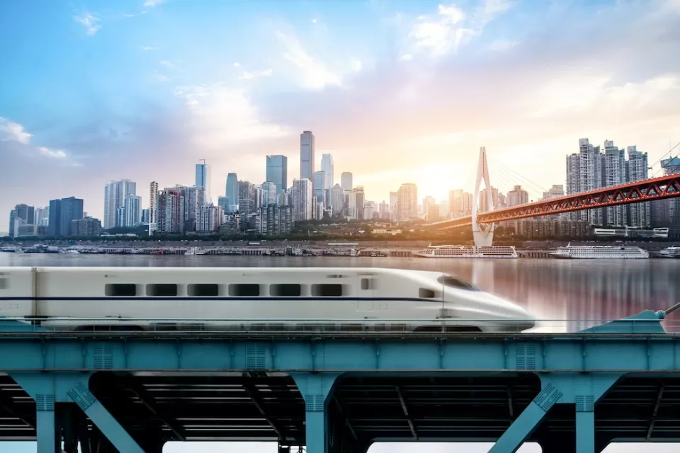 High-speed rail train passing on bridge with Chongqing, China skyline in background.